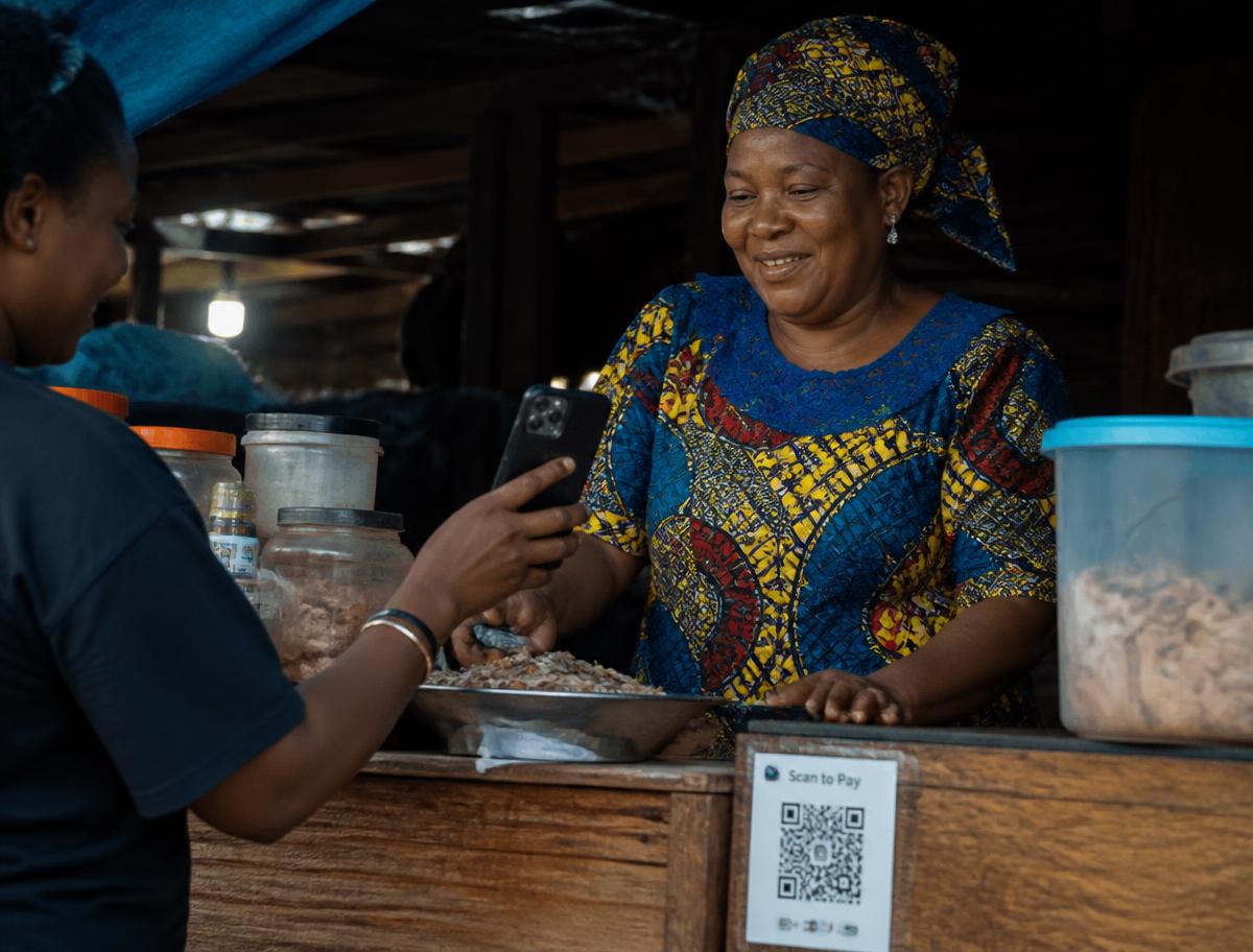 A Nigerian market vendor receiving a payment via a printed QR code at her stall